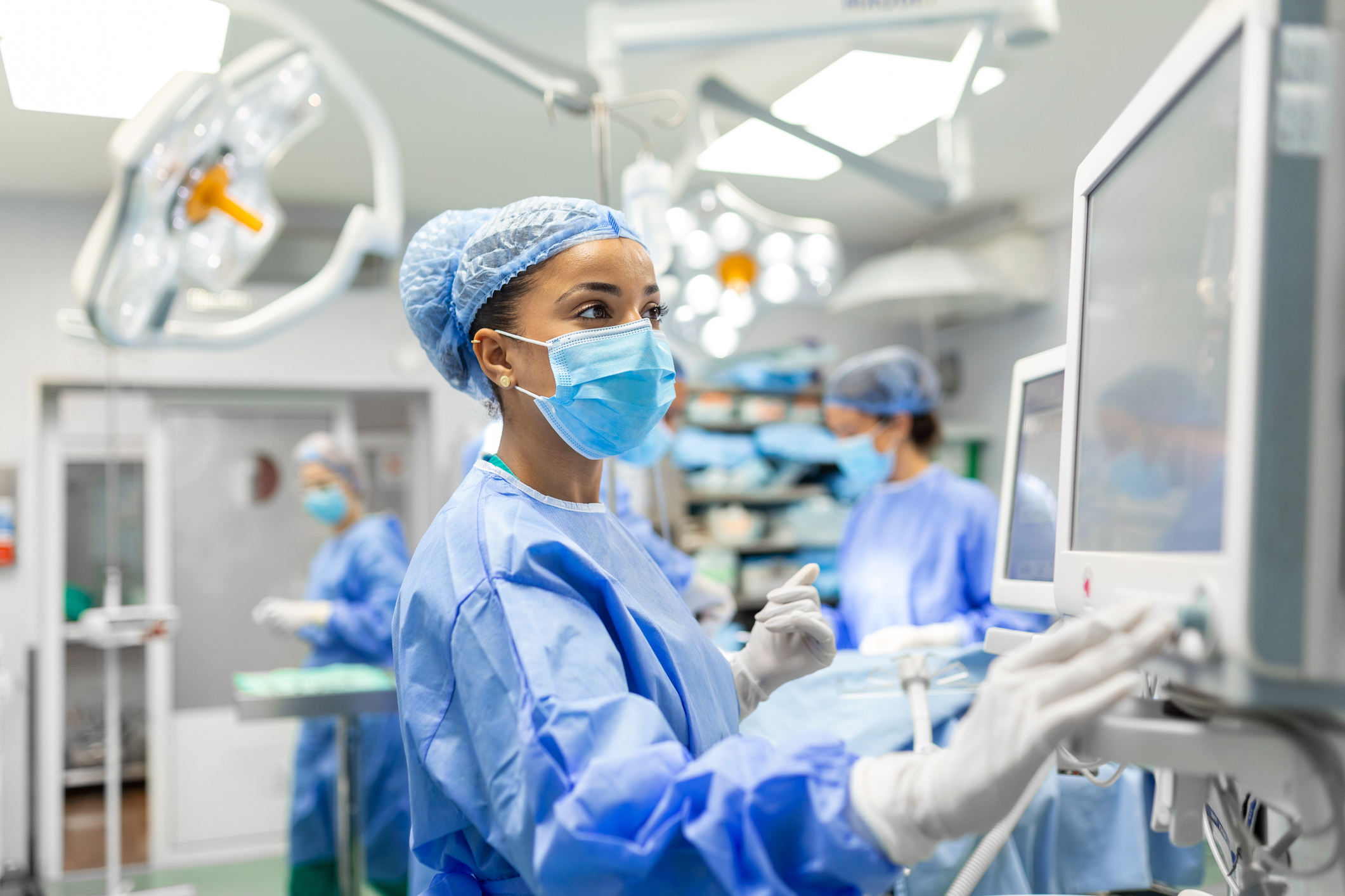 Anesthetist Working In Operating Theatre Wearing Protecive Gear checking monitors while sedating patient before surgical procedure in hospital Anesthetist Working In Operating Theatre Wearing Protecive Gear checking monitors while sedating patient before surgical procedure in hospital